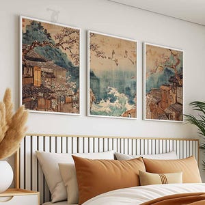 May include: Three framed prints of Japanese art depicting traditional houses and landscapes. The prints are in a white frame and are hung on a white wall.