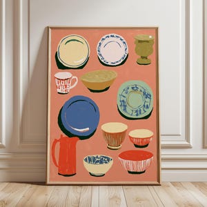 May include: A rectangular wall art print featuring a collection of illustrated kitchenware on a terracotta background. The artwork displays various plates, bowls, a mug, a pitcher, and a vase in blue, red, yellow, green, and white colors.