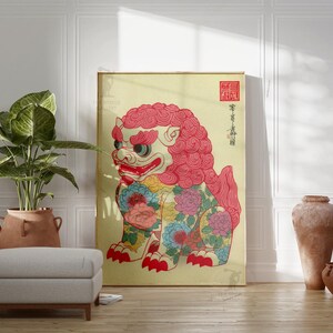 May include: A framed artwork featuring a colorful, stylized lion-dog with a red mane and floral patterns. The artwork has Japanese text and a red seal. The artwork is displayed in a room with a plant, ottoman, and decorative vases.