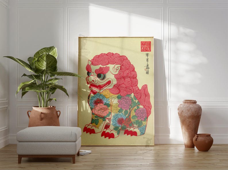 May include: A framed artwork featuring a colorful, stylized lion-dog with a red mane and floral patterns. The artwork has Japanese text and a red seal. The artwork is displayed in a room with a plant, ottoman, and decorative vases.