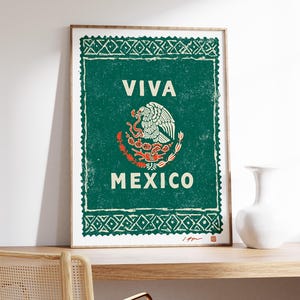May include: Framed print featuring the Mexican coat of arms, with a green background and white text that reads "VIVA MEXICO." The artwork has a distressed, vintage aesthetic, with a wooden frame.