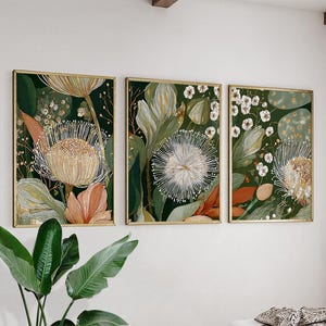 May include: A triptych of framed botanical art prints. Each print showcases detailed illustrations of stylized flowers and foliage in green, cream, and peach hues, set against a dark green backdrop. The frames have a gold finish.