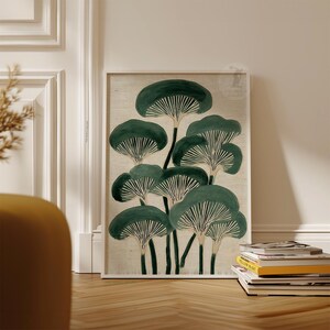 May include: A framed art print featuring a stylized illustration of dark green mushrooms with white gills against a beige background. The artwork is displayed on a wooden floor, leaning against a white wall.