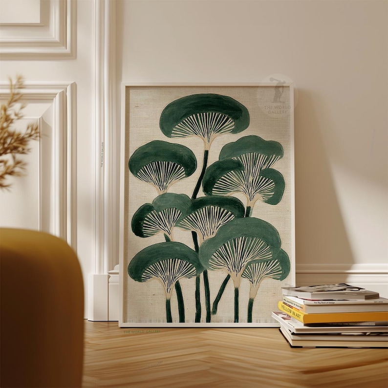 May include: A framed art print featuring a stylized illustration of dark green mushrooms with white gills against a beige background. The artwork is displayed on a wooden floor, leaning against a white wall.