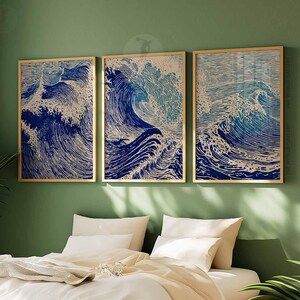 May include: Three framed art prints depicting stylized ocean waves in shades of blue and white. The artwork is displayed on a green wall above a bed with white bedding. The frames have a gold finish. The text "THE WORLD GALLERY" is visible.