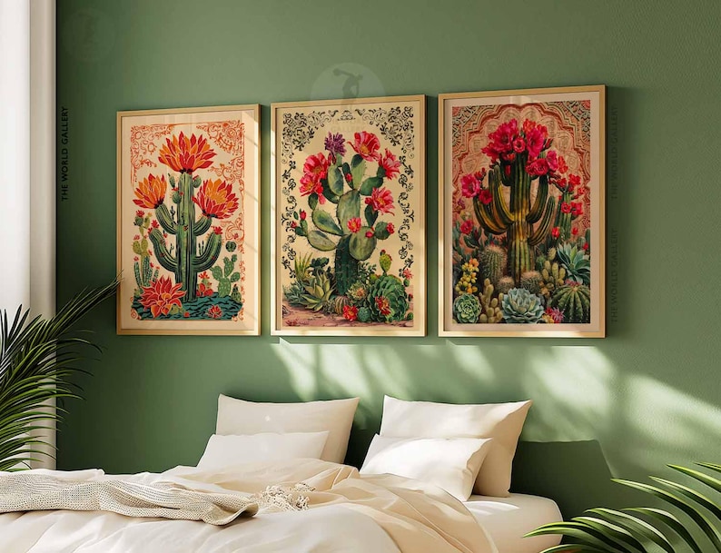 May include: Three framed botanical prints featuring illustrations of cacti with red and pink flowers. The prints are set against a green wall and above a bed with white linens.