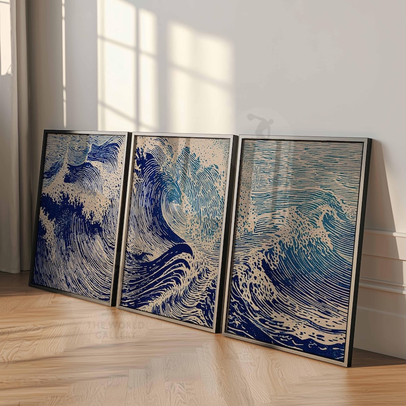 May include: Three framed art prints depicting ocean waves in shades of blue and beige. The artwork has a woodcut style, with detailed lines creating the wave patterns. The frames are black, and the prints are leaning against a white wall.
