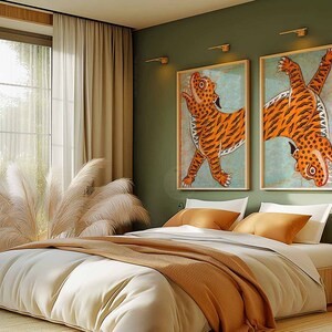 May include: A bedroom with a white bed with a brown blanket and two white pillows. There are two framed pictures of tigers on the wall behind the bed. The walls are a sage green color. There are two lamps on the wall and a small table with a lamp on it.