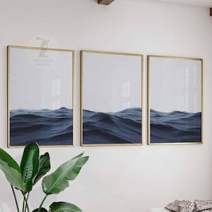 Könnte beinhalten: Drei gerahmte Kunstdrucke mit einer ruhigen Meereslandschaft. Jeder Druck zeigt dunkelblaue Wellen unter einem blassen Himmel, mit einem goldfarbenen Rahmen. Der Text "THE WORLD GALLERY" ist auf dem linken Druck sichtbar. Das Kunstwerk wird an einer weißen Wand ausgestellt.