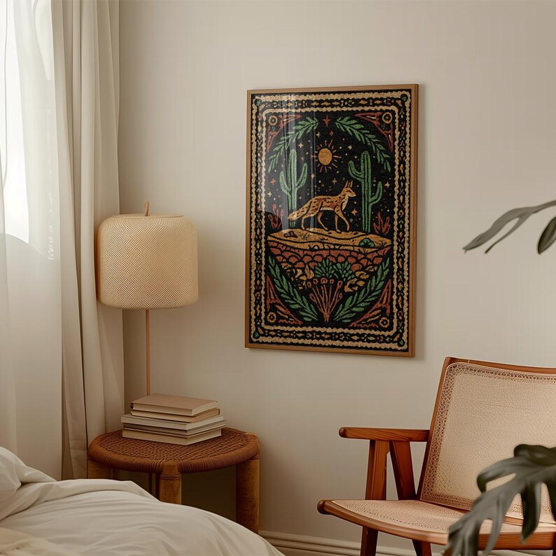 May include: A framed art print featuring a desert landscape with a fox, cacti, and a sun. The artwork has a dark background with green, red, and orange accents. The frame is a light brown color.