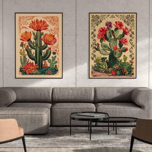 Op de afbeelding: Twee vintage botanische illustraties van cactussen met rode bloemen. De illustraties zijn in zwart ingelijst en worden weergegeven op een muur boven een grijze bank.