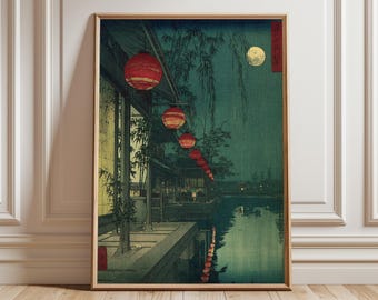 Op de afbeelding: Ingelijste prent van een Japans landschap 's nachts. Het kunstwerk toont een waterkant met rode lantaarns, een volle maan en reflecties in het water. Het kleurenpalet wordt gedomineerd door groen, blauw en rood, wat een serene sfeer creëert.