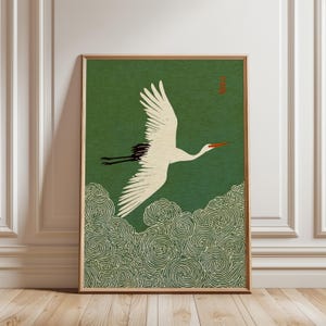 May include: A framed print depicting a white crane in flight against a green backdrop. The crane has black wingtips and a red beak. Swirling cloud patterns are at the bottom, and a red Japanese character is in the upper right corner.