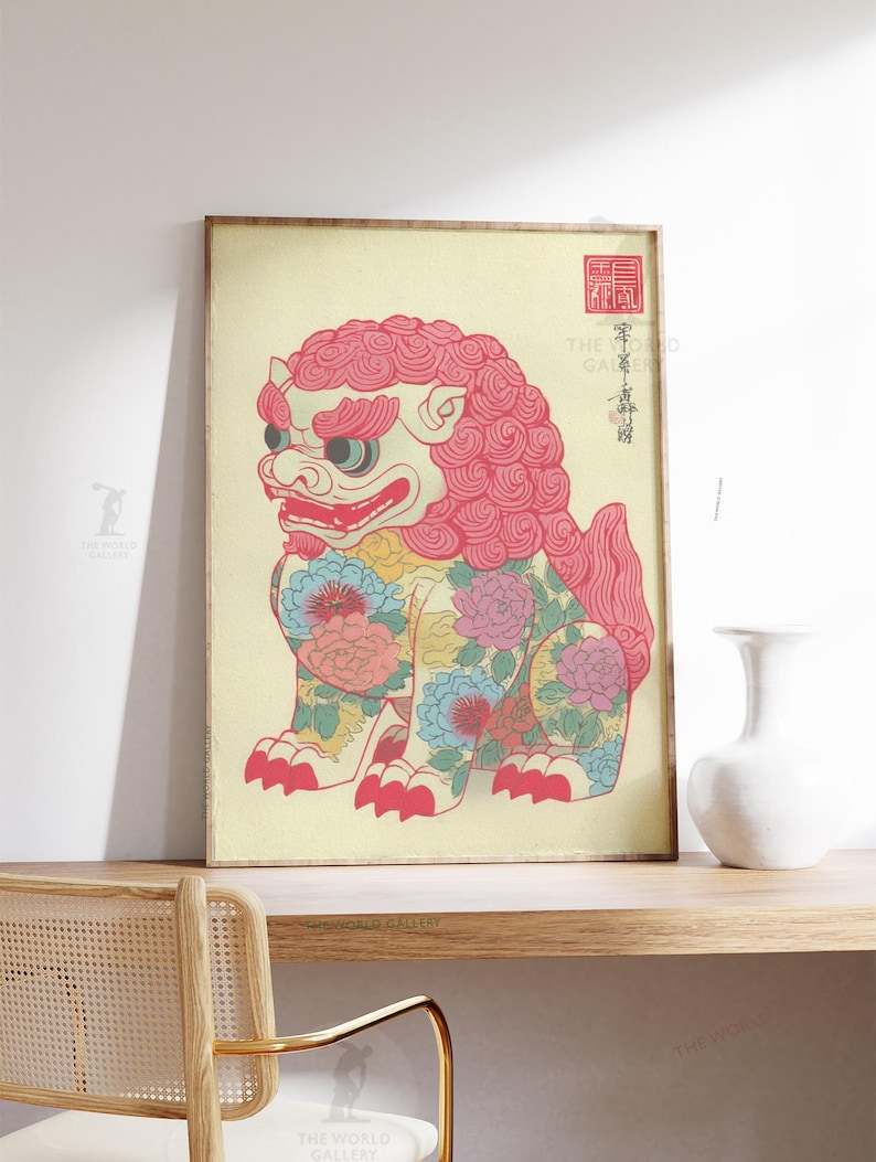 May include: Framed print of a stylized, seated lion-like creature with a pink mane and floral patterns. The artwork features a cream-colored background and traditional Japanese text and seals. The frame is a light brown color.