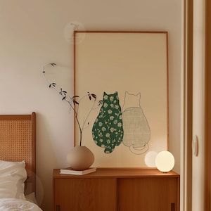 Puede incluir: Una impresi&oacute;n art&iacute;stica enmarcada con dos gatos estilizados. Uno es verde con un estampado floral blanco, el otro est&aacute; delineado en negro con un patr&oacute;n de cuadros. La obra de arte se muestra sobre un fondo beige claro.