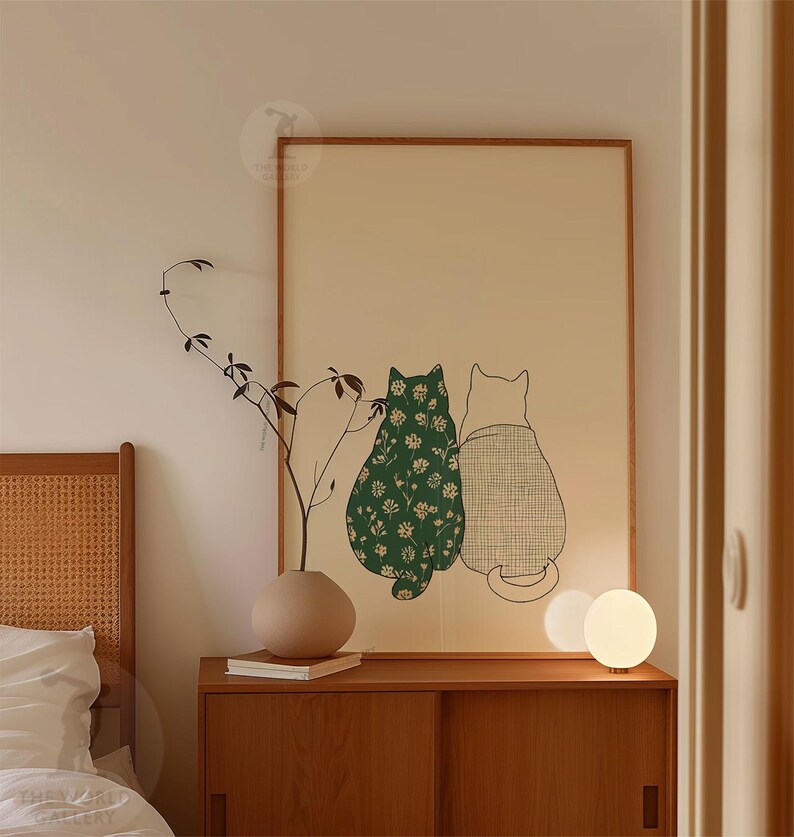 Puede incluir: Una impresi&oacute;n art&iacute;stica enmarcada con dos gatos estilizados. Uno es verde con un estampado floral blanco, el otro est&aacute; delineado en negro con un patr&oacute;n de cuadros. La obra de arte se muestra sobre un fondo beige claro.