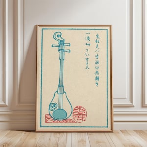 May include: A framed print featuring a traditional Japanese stringed instrument, rendered in shades of blue and red against a cream background. The artwork includes Japanese text and a decorative seal, framed in a wooden border.