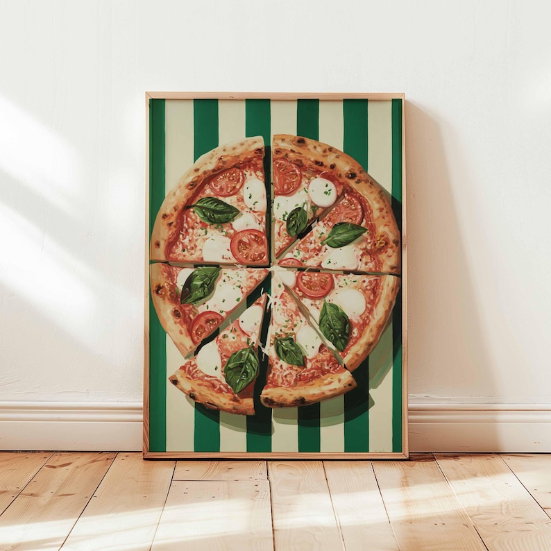 May include: A framed print of a pizza, cut into slices, with tomatoes, mozzarella, and basil. The pizza is set against a green and white striped background. The frame is a light brown color. The image is displayed on a wooden floor.