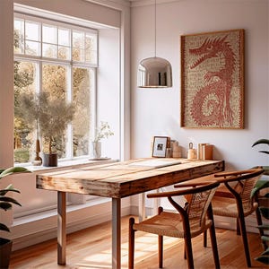 May include: A rustic wooden desk with metal legs and two woven chairs. A framed red dragon art piece hangs on the wall. A large window with a view of trees and a silver pendant light complete the room's decor.