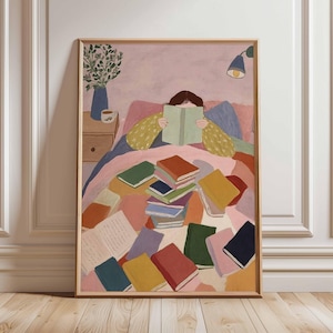 May include: A framed art print depicts a person reading in bed, surrounded by colorful books. The illustration features a soft color palette with a pink background, a wooden nightstand, and a blue vase with greenery.