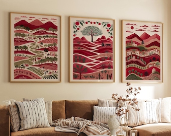 May include: Three framed rectangular wall art prints featuring stylized landscape illustrations in shades of red, pink, and green. The artwork depicts rolling hills, trees, small buildings, and figures in a repeating, decorative pattern.