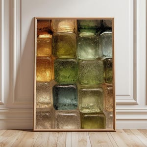 Könnte beinhalten: Ein gerahmtes Kunstwerk mit einem Mosaik aus quadratischen Glasblöcken in den Farbtönen Bernstein, Grün und Blau. Die Glasblöcke haben eine strukturierte Oberfläche, die ein Spiel von Licht und Schatten erzeugt. Das Kunstwerk wird in einem Raum mit weißen Paneelen und Holzboden ausgestellt.