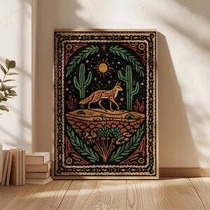 May include: A framed art print featuring a desert landscape with a fox, cacti, and sun. The artwork has a black background with green, orange, and yellow accents. The fox is brown and orange, and the cacti are green. The print is in a wooden frame.