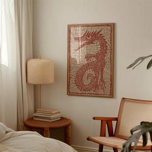 May include: A framed print featuring a red dragon illustration. The artwork has a textured appearance with a light background and a wooden frame. The dragon is depicted in a stylized, detailed manner, with a focus on its sharp teeth and curled tail.