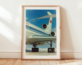 May include: Framed print of a vintage airplane against a blue sky with clouds. The aircraft is white and silver with red accents on the tail. The plane's engines are visible, and the landing gear is down. The image is set in a wooden frame.