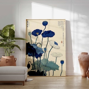 May include: A framed art print featuring a botanical illustration of blue and white poppies with green leaves against a cream background. The artwork has Japanese text and is displayed in a room with a plant, ottoman, and pottery.