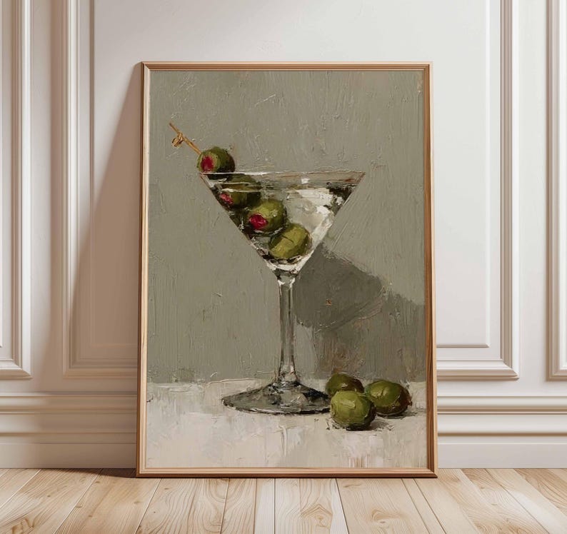May include: A framed painting of a martini glass filled with olives. The artwork features a clear glass with a stem, filled with a clear liquid and green olives. The background is a muted gray, and the painting is in a wooden frame.