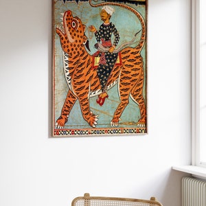 May include: A vintage illustration of a man riding a tiger. The man is wearing a turban and a long robe. The tiger is orange and black with a blue background. The illustration is framed in a wooden frame.