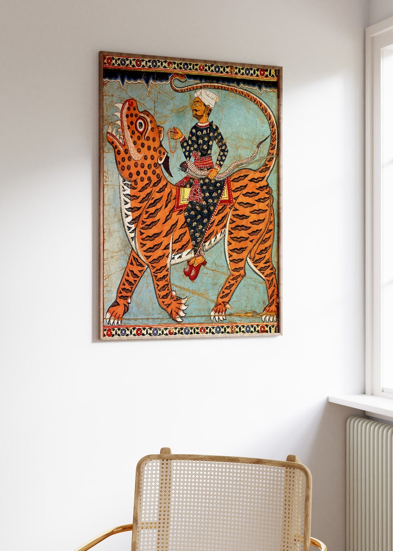 May include: A vintage illustration of a man riding a tiger. The man is wearing a turban and a long robe. The tiger is orange and black with a blue background. The illustration is framed in a wooden frame.