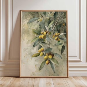 May include: A framed watercolour painting of an olive branch, featuring green leaves and yellow-green olives. The frame is light brown wood. The background has a soft, textured, neutral colour palette.