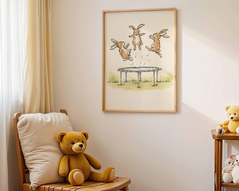 May include: A framed print featuring a whimsical illustration of three brown rabbits jumping on a trampoline. The artwork is set against a backdrop of a grassy field and a light-colored sky. The frame is made of light-colored wood. A teddy bear sits on a wooden chair.