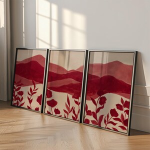 May include: Three framed art prints featuring a watercolor landscape with red mountains and floral accents. The artwork has a neutral background with red flowers and foliage at the bottom. The frames are black.