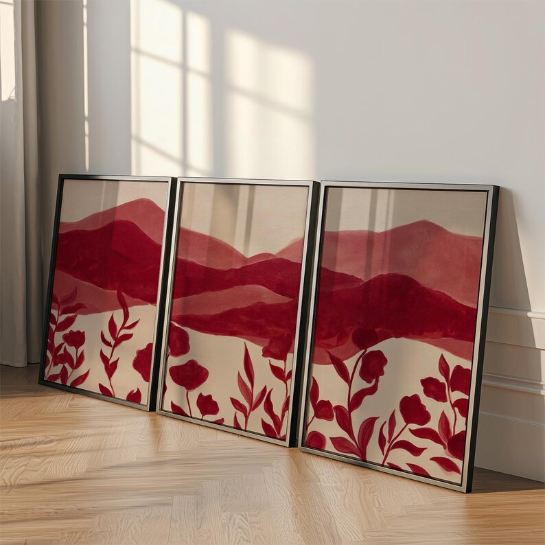 May include: Three framed art prints featuring a watercolor landscape with red mountains and floral accents. The artwork has a neutral background with red flowers and foliage at the bottom. The frames are black.