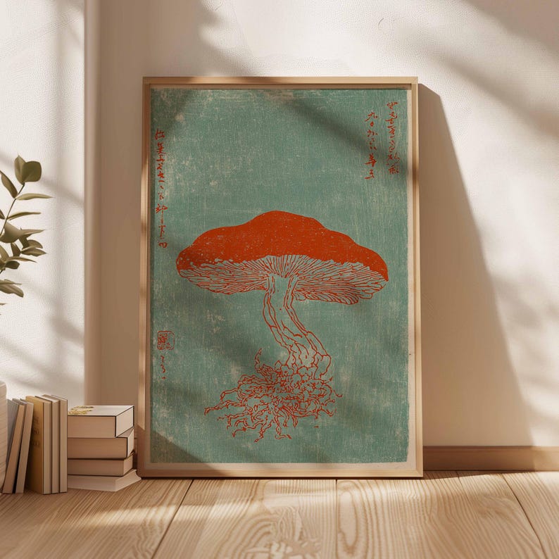 May include: A framed print featuring a stylized orange mushroom illustration against a teal background. The artwork has Japanese text and a woodblock print aesthetic. The print is displayed in a light-colored wooden frame.