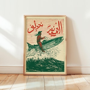 Könnte beinhalten: Ein gerahmter rechteckiger Druck mit einer rot-grünen Illustration einer Person, die auf einem großen Fisch über stilisierten Wellen reitet. Das Kunstwerk enthält rote arabische Schriftzeichen auf cremefarbenem Grund in einem Holzrahmen.