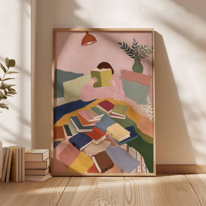 May include: A framed art print depicts a person reading a book surrounded by colorful books and pillows. The artwork features a warm color palette with pink, blue, green, and yellow hues. A small orange lamp hangs above the person, and a vase of greenery is visible.