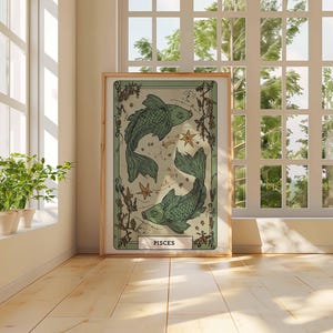 May include: A framed art print featuring a Pisces zodiac illustration. The artwork depicts two green fish swimming in opposite directions, with stars and botanical elements. The print has a light green and beige color palette and is displayed in a room with natural light.