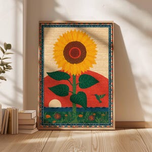 Op de afbeelding: Een ingelijste kunstdruk met een grote gele zonnebloem met een bruin centrum, tegen een rode zonsondergang. Groene bladeren en een kolibrie zijn ook zichtbaar. De print heeft een decoratieve rand en is in een houten lijst.