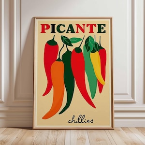 May include: A framed art print featuring a collection of stylized chili peppers in red, orange, green, and yellow against a beige background. The word "PICANTE" is printed in red, green, and black above the peppers, with "chillies" in black below.