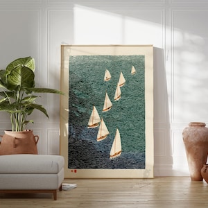 May include: A framed print of sailboats on a teal ocean. The artwork features several white sailboats with tan sails against a textured background. The print is displayed in a room with a plant, ottoman, and decorative vases.
