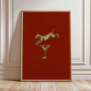Pu&ograve; includere: Stampa artistica incorniciata con un cane color oro che salta sopra un bicchiere da martini. Il cane e il bicchiere sono posti su uno sfondo rosso intenso. L'opera d'arte &egrave; esposta in una cornice di legno, adatta all'arredamento della casa.