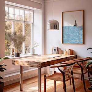 May include: A bright, airy room with a wooden desk and two chairs. A framed sailboat art print hangs on the wall. A large window offers a view of trees. A silver pendant light hangs above the desk.