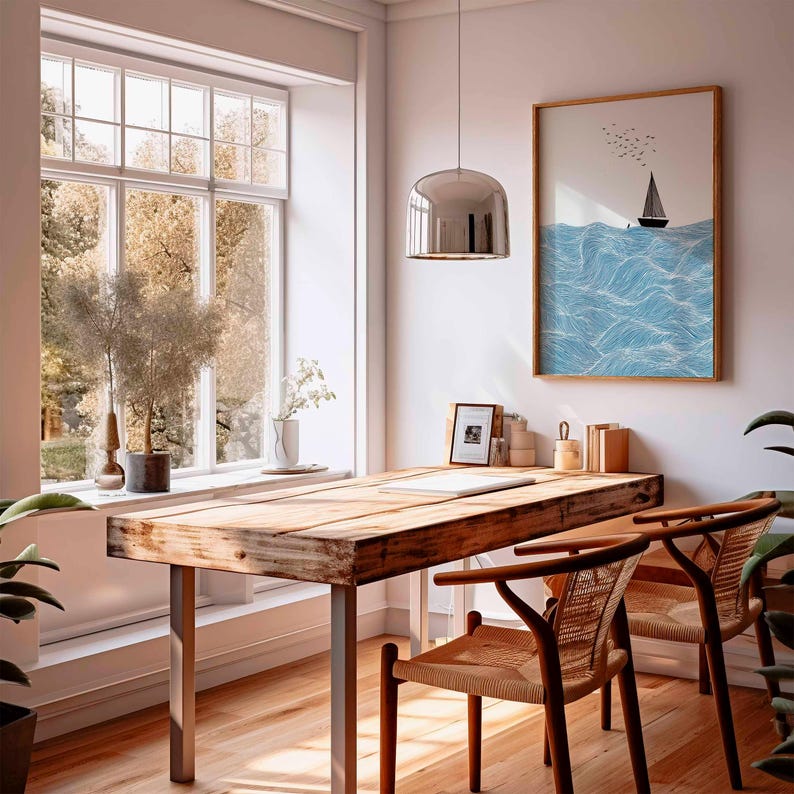 May include: A bright, airy room with a wooden desk and two chairs. A framed sailboat art print hangs on the wall. A large window offers a view of trees. A silver pendant light hangs above the desk.
