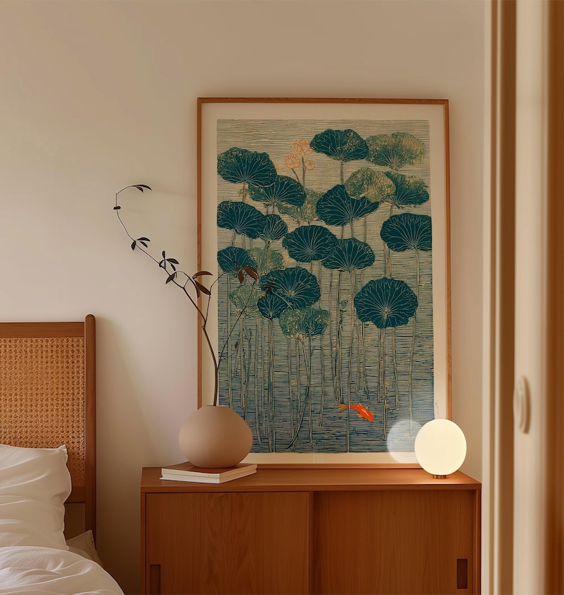 May include: A framed art print featuring a teal and green lotus pond scene with a small orange fish. The artwork is displayed above a wooden cabinet with a round beige vase and a small lamp.