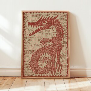May include: A framed print featuring a stylized red dragon illustration. The dragon is depicted with sharp teeth, claws, and a curled tail, set against a textured beige background. The artwork is enclosed in a natural wood frame, suitable for wall decor.