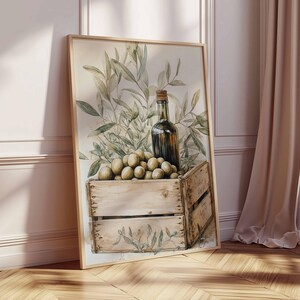 May include: Watercolor print of a still life featuring a wooden crate filled with olives, a dark glass bottle, and olive branches. The artwork has a neutral color palette with a rustic aesthetic, perfect for kitchen or dining room decor.